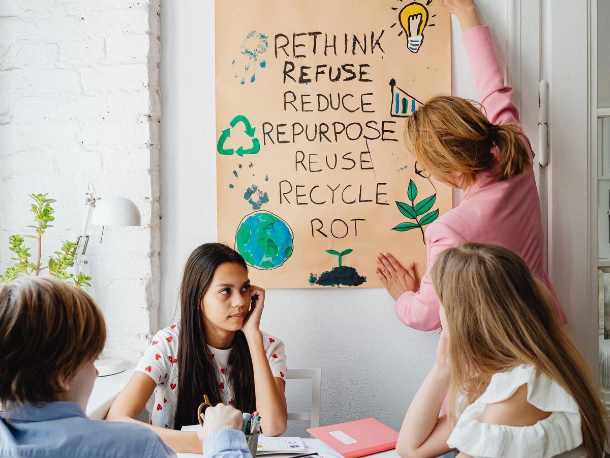 Teens working together at a table while an adult hangs a hand-painted Zero Waste poster